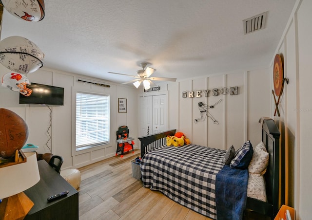 bedroom featuring a closet, light hardwood / wood-style floors, ceiling fan, and a textured ceiling