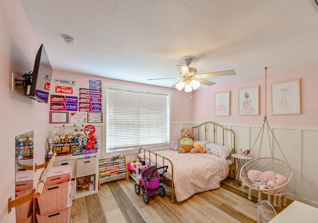 bedroom featuring light hardwood / wood-style floors, ceiling fan, and a textured ceiling