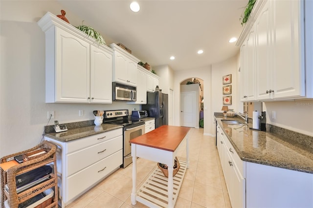 kitchen featuring appliances with stainless steel finishes, light tile floors, sink, white cabinetry, and dark stone countertops