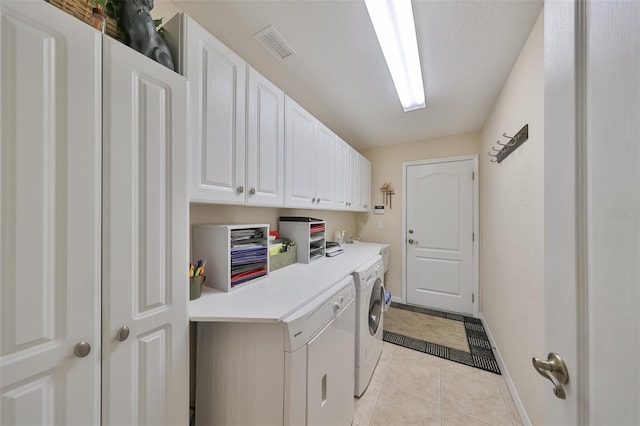 clothes washing area featuring washing machine and dryer, cabinets, and light tile flooring