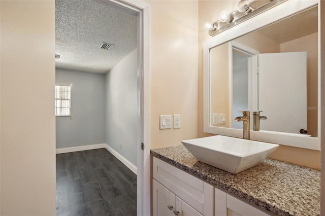 bathroom with a textured ceiling, wood-type flooring, and vanity with extensive cabinet space