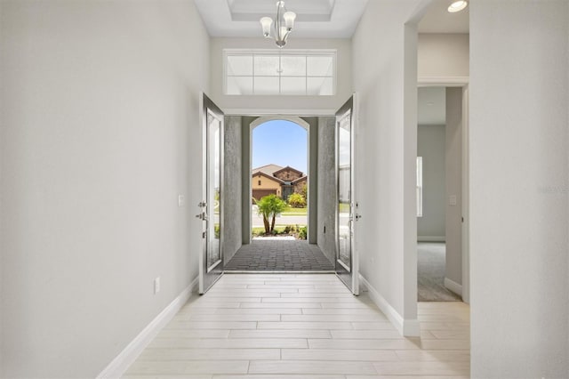 entryway featuring a chandelier, a tray ceiling, light wood-style floors, and baseboards