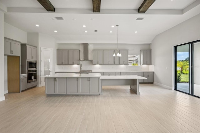 kitchen featuring appliances with stainless steel finishes, a kitchen island with sink, gray cabinets, and wall chimney range hood