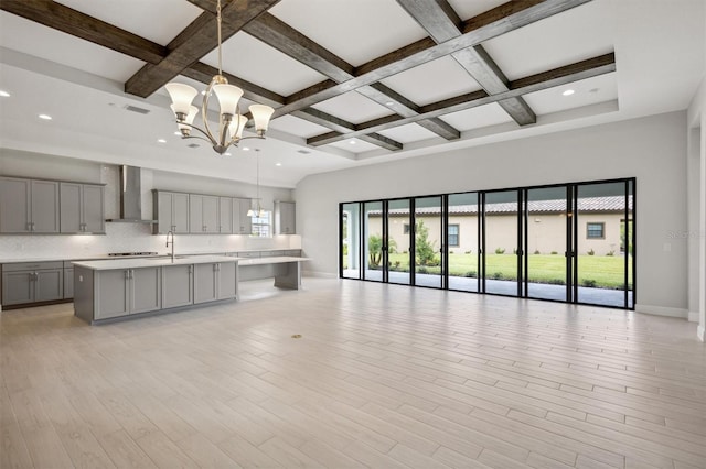 kitchen featuring a notable chandelier, open floor plan, light countertops, wall chimney range hood, and gray cabinets