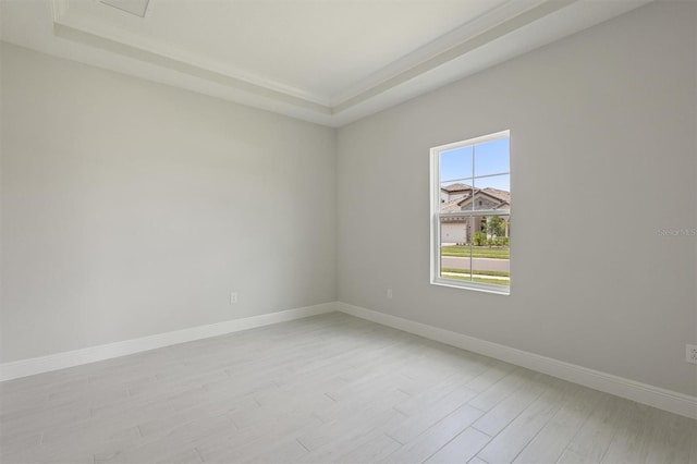 empty room with light wood-style floors, a raised ceiling, and baseboards