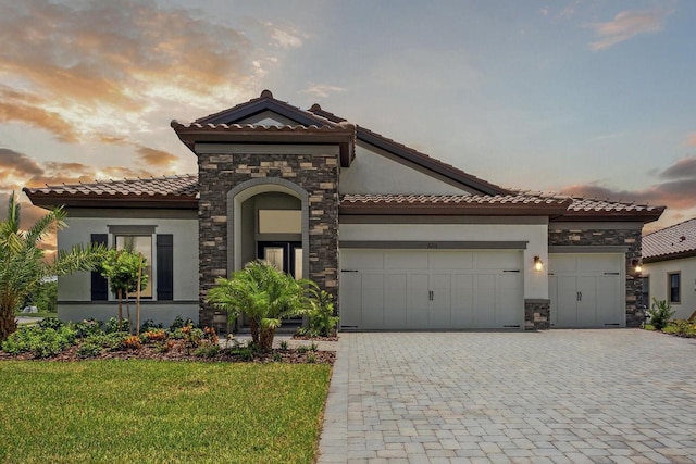 mediterranean / spanish house featuring decorative driveway, stone siding, and stucco siding