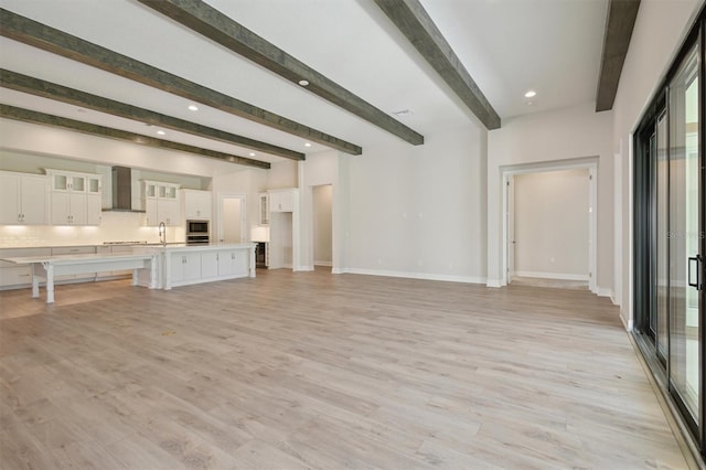 unfurnished living room with sink, beamed ceiling, and light wood-type flooring