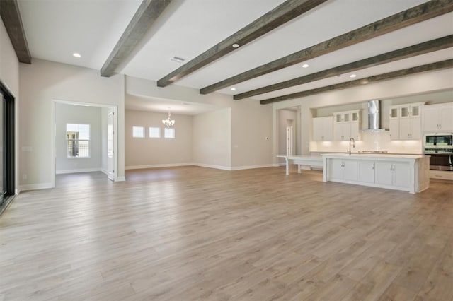 unfurnished living room featuring beam ceiling, light wood-type flooring, an inviting chandelier, and sink