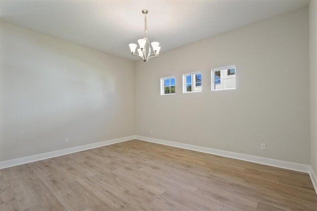 spare room with a notable chandelier and light hardwood / wood-style floors