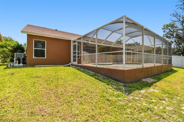 rear view of house featuring glass enclosure and a lawn