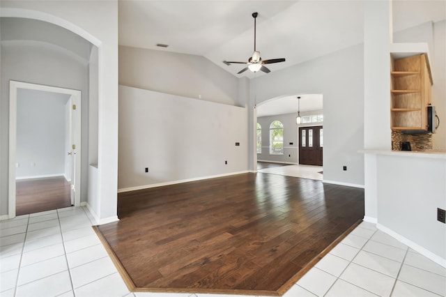 unfurnished living room with high vaulted ceiling, ceiling fan, and light tile flooring