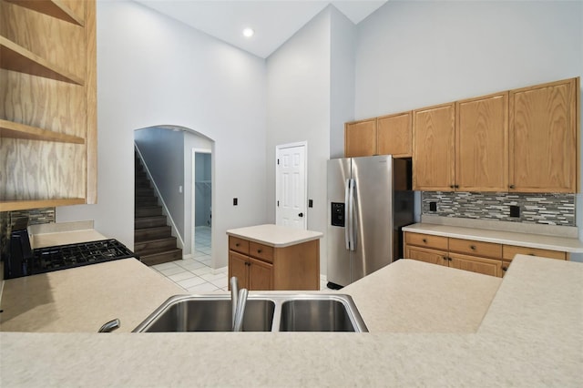 kitchen featuring high vaulted ceiling, stainless steel refrigerator with ice dispenser, light tile flooring, backsplash, and sink