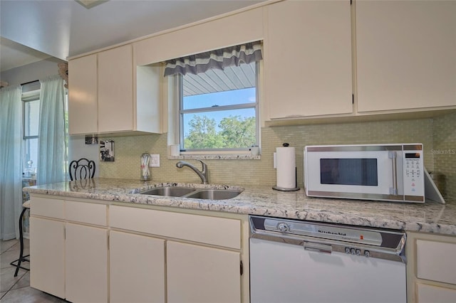 kitchen featuring dishwashing machine, tasteful backsplash, light stone counters, sink, and tile floors