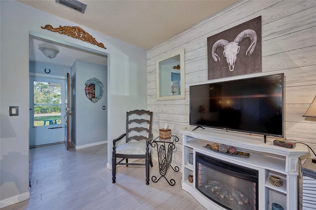 living room with light hardwood / wood-style flooring, wood walls, and a textured ceiling