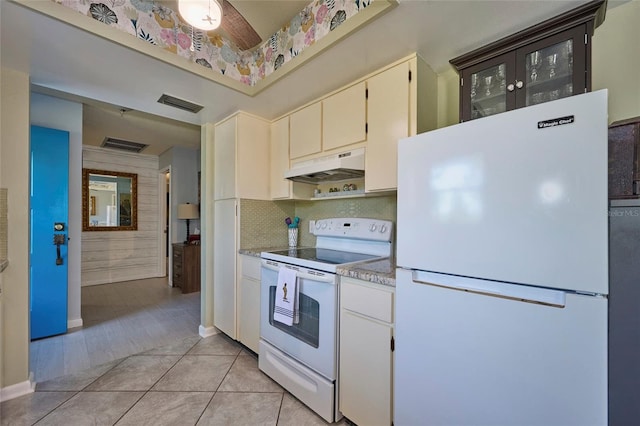 kitchen featuring white appliances, white cabinetry, backsplash, wall chimney range hood, and light tile floors