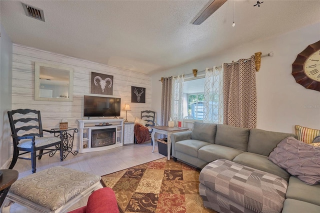 living room featuring ceiling fan, a fireplace, a textured ceiling, hardwood / wood-style floors, and wooden walls