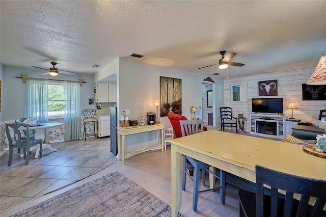 dining area featuring wood walls, a textured ceiling, ceiling fan, and light tile floors