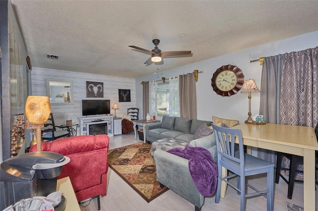 living room featuring hardwood / wood-style floors, ceiling fan, wood walls, and a textured ceiling