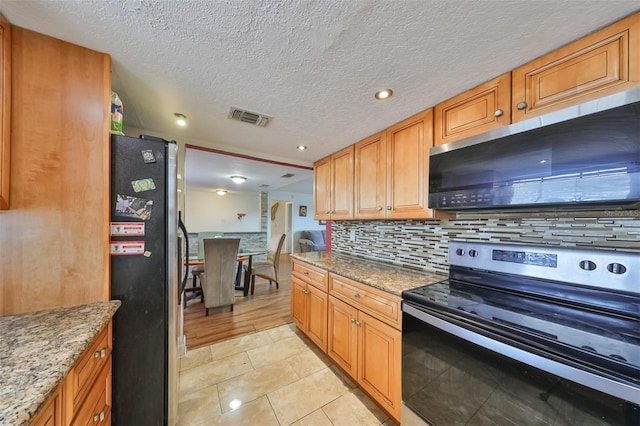 kitchen with stainless steel appliances, tasteful backsplash, light stone counters, light tile patterned floors, and a textured ceiling