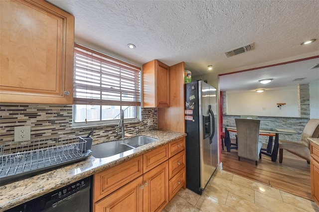 kitchen featuring dishwasher, light stone counters, stainless steel refrigerator with ice dispenser, light tile patterned floors, and sink