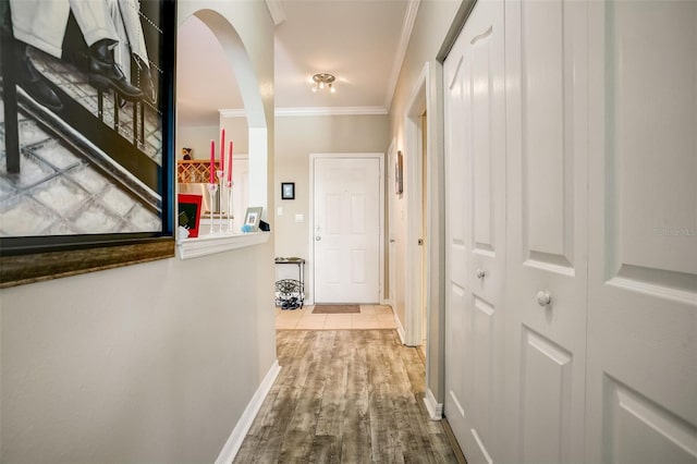 corridor with crown molding, wood finished floors, arched walkways, and baseboards