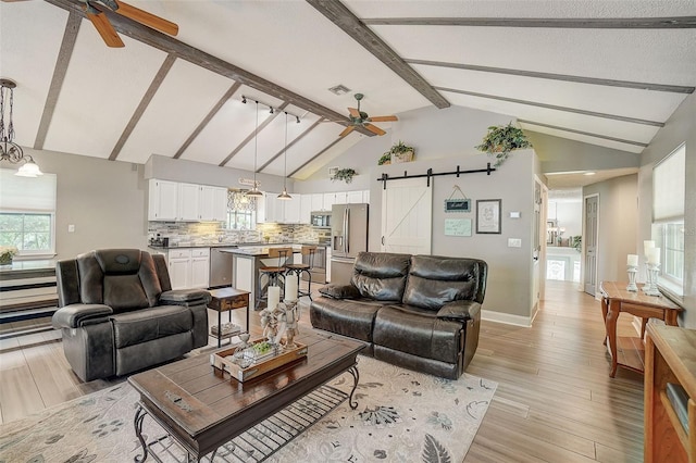 living room with ceiling fan, beamed ceiling, light wood-type flooring, a barn door, and high vaulted ceiling