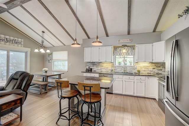 kitchen with beamed ceiling, light wood-type flooring, a center island, white cabinets, and appliances with stainless steel finishes