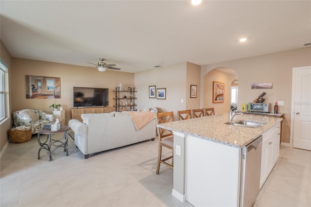 kitchen with white cabinets, sink, stainless steel dishwasher, an island with sink, and light stone countertops