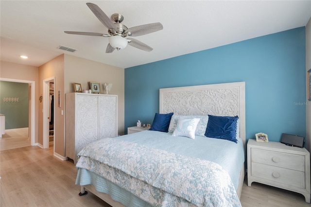 bedroom featuring light hardwood / wood-style flooring, ceiling fan, a walk in closet, and a closet