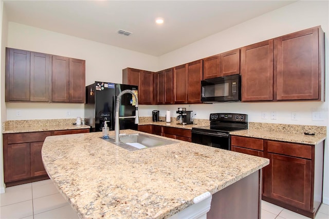 kitchen featuring light stone countertops, sink, black appliances, and an island with sink