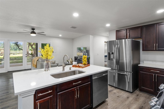 kitchen with stainless steel appliances, french doors, an island with sink, sink, and light wood-type flooring