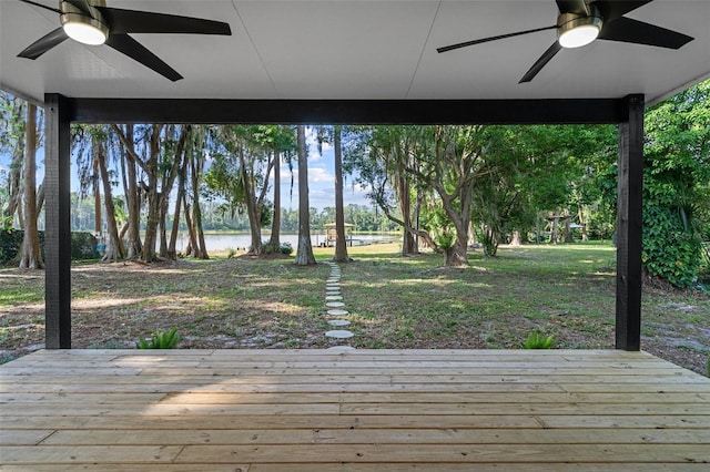 wooden deck with a water view, ceiling fan, and a lawn