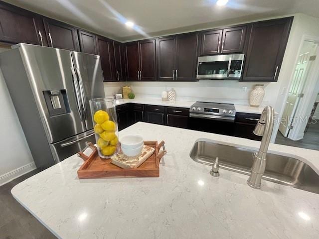 kitchen featuring light stone countertops, stainless steel appliances, dark brown cabinets, and sink