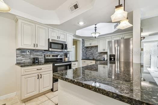 kitchen with appliances with stainless steel finishes, decorative light fixtures, a tray ceiling, and dark stone countertops