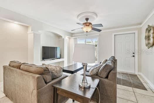 tiled living room with ceiling fan and ornamental molding