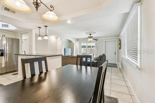 dining space with ceiling fan, a raised ceiling, and light tile patterned floors