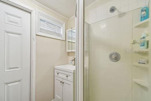 bathroom with a shower with door, vanity, and crown molding