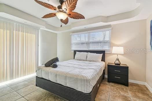 tiled bedroom with a raised ceiling and ceiling fan