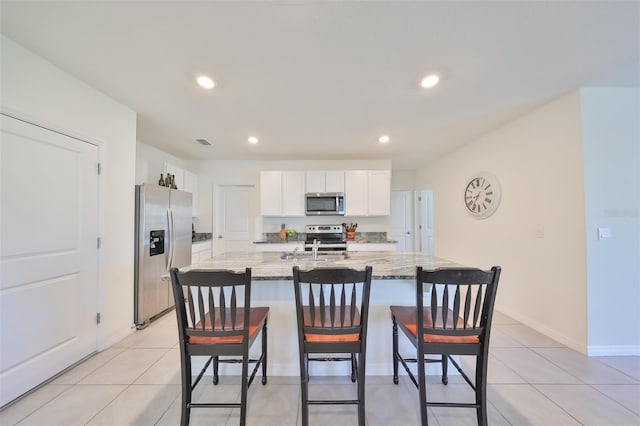 kitchen featuring white cabinetry, an island with sink, light stone countertops, appliances with stainless steel finishes, and a kitchen bar