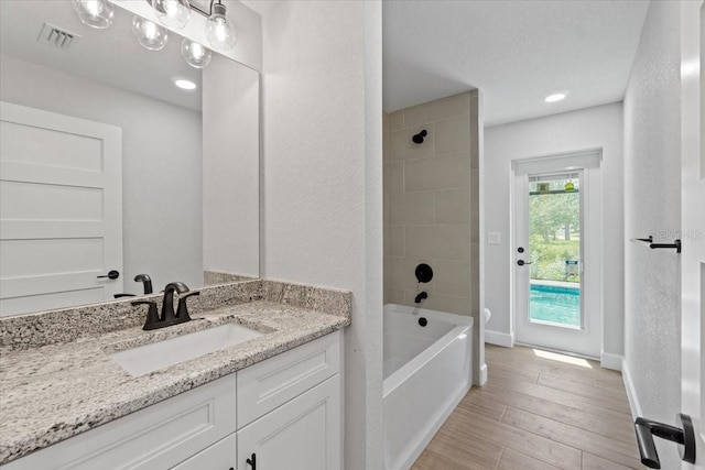 bathroom with tiled shower / bath combo, hardwood / wood-style flooring, and vanity