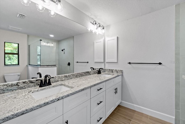 bathroom featuring toilet, vanity, a textured ceiling, and a tile shower