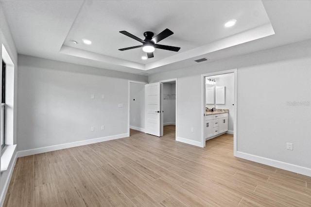 unfurnished bedroom featuring ceiling fan, connected bathroom, light hardwood / wood-style flooring, and a tray ceiling