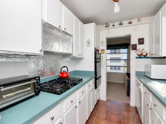 kitchen with white appliances, tasteful backsplash, dark tile flooring, white cabinets, and sink