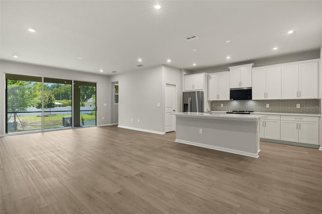 kitchen featuring light hardwood / wood-style flooring, an island with sink, stainless steel appliances, decorative backsplash, and white cabinets