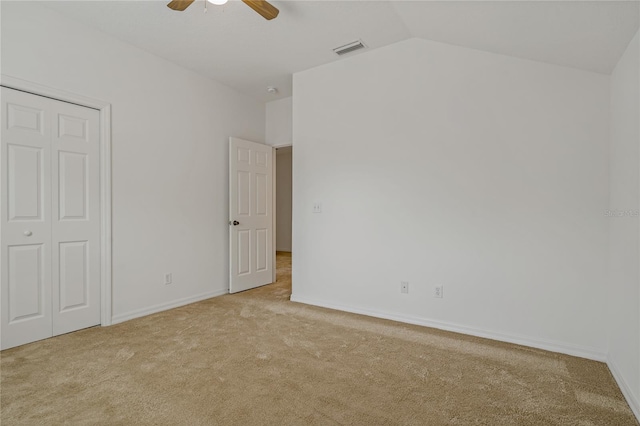 unfurnished bedroom featuring ceiling fan, light colored carpet, vaulted ceiling, and a closet