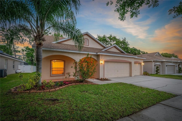 view of front of home with a garage, a yard, and central air condition unit