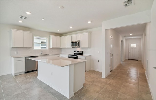 kitchen featuring white cabinetry, sink, tasteful backsplash, a kitchen island, and appliances with stainless steel finishes