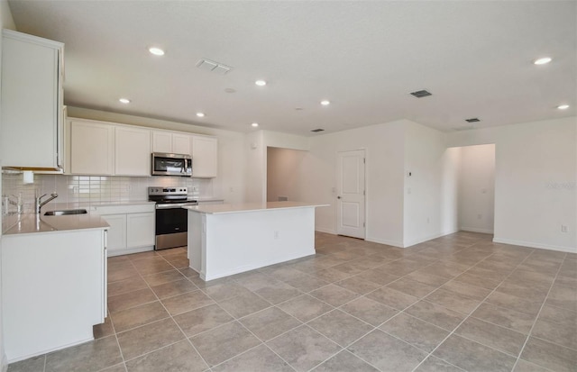 kitchen featuring white cabinets, decorative backsplash, light tile patterned floors, a kitchen island, and stainless steel appliances