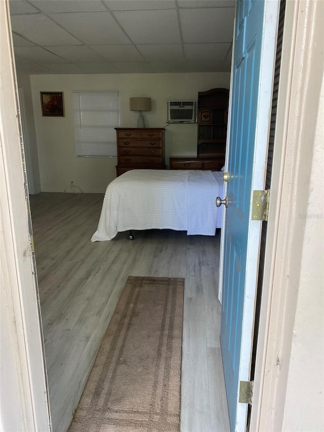 bedroom featuring an AC wall unit, hardwood / wood-style flooring, and a paneled ceiling