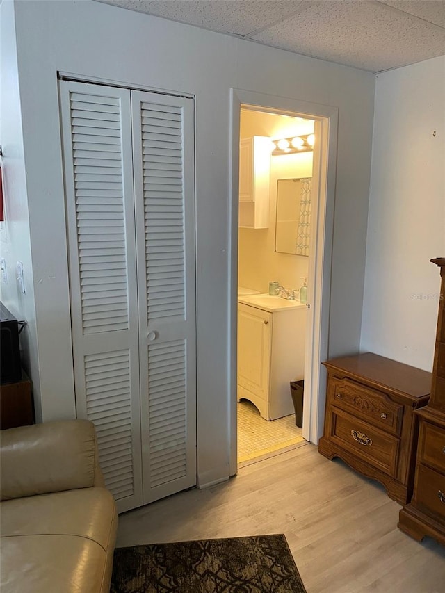 bedroom with a closet, a paneled ceiling, connected bathroom, sink, and light wood-type flooring